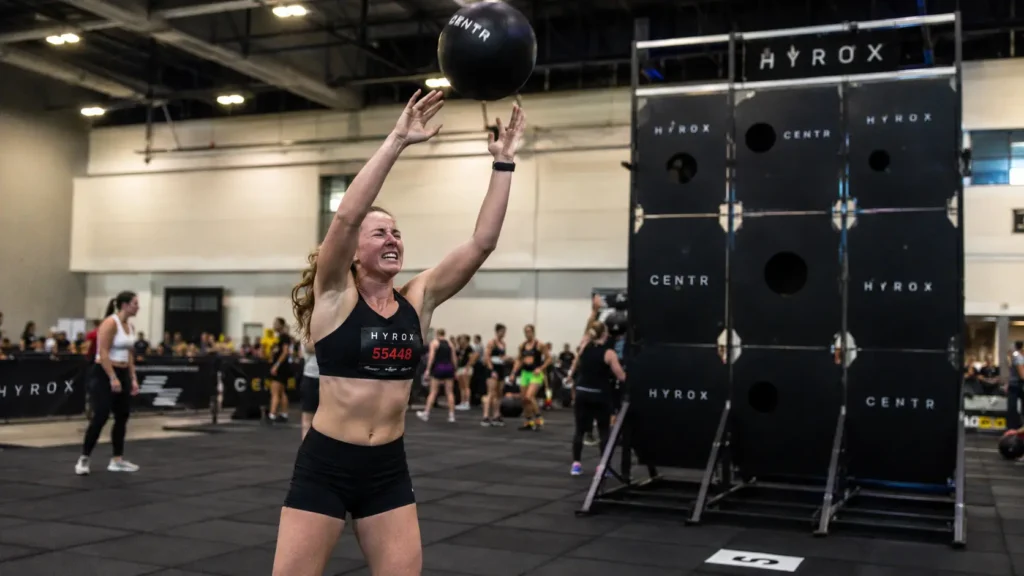 Female HYROX athlete performing wall balls at station 8 where wearing a lifting belt for HYROX restricts breathing