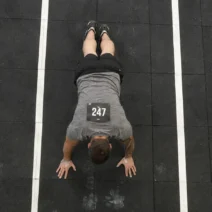 how to train burpee broad jumps for HYROX — athlete in plank position on rubber floor during station 4